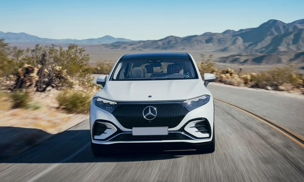Фото Mercedes-Benz EQS SUV (2024) — вид спереди, фото 10. Белый кузов, строгая симметрия оптики — базовый ракурс знакомства с дизайном. Рисунок ходовых огней — подпись модели, по нему её узнают в потоке Mercedes-Benz EQS SUV (2024) — вид спереди, фото 10