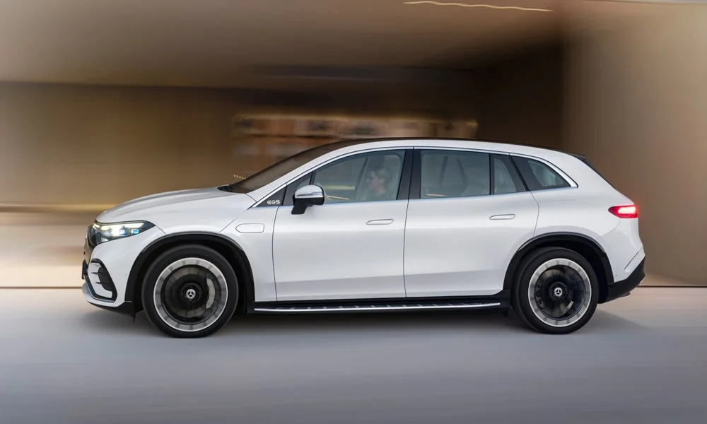 Фото Mercedes-Benz EQS SUV (2024) — вид сбоку, фото 2. Сбоку читаются линия остекления и характер выштамповок на белом кузове. Хромированные или чёрные молдинги окон отличают комплектации Mercedes-Benz EQS SUV (2024) — вид сбоку, фото 2