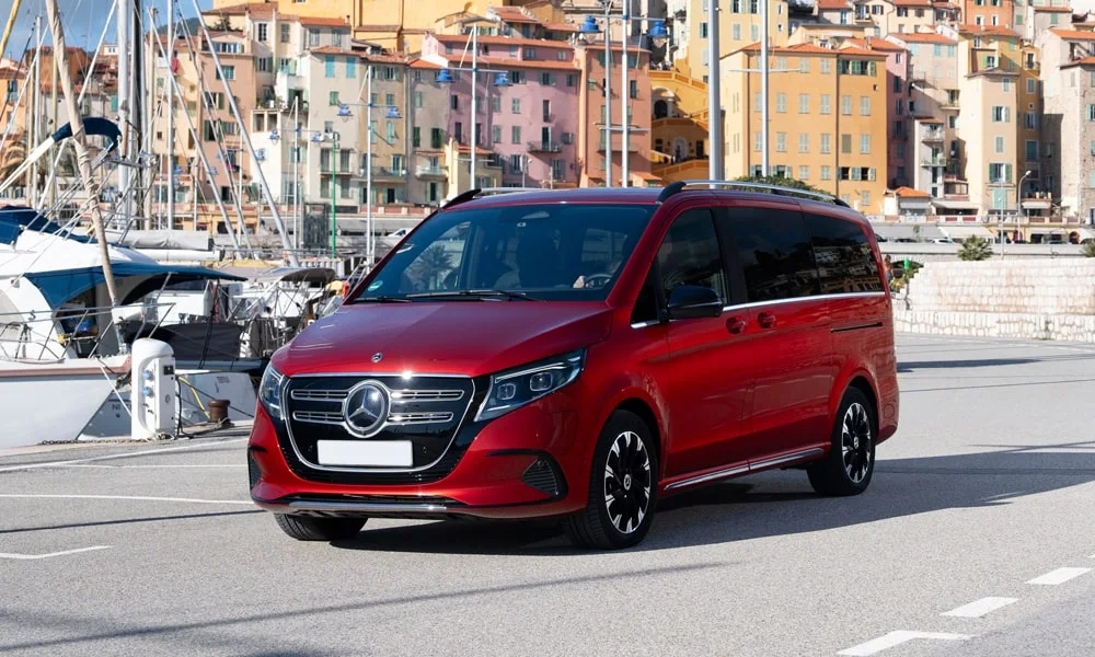 Фото Mercedes-Benz EQV (2024) — вид спереди, фото 7. Красный кузов, строгая симметрия оптики — базовый ракурс знакомства с дизайном. Рисунок ходовых огней — подпись модели, по нему её узнают в потоке Mercedes-Benz EQV (2024) — вид спереди, фото 7