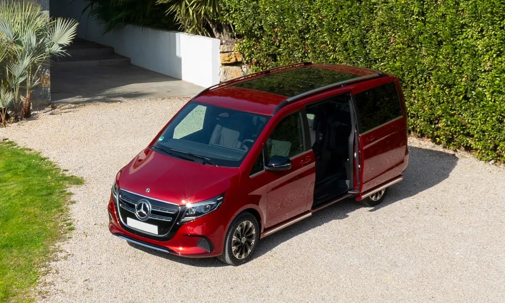 Фото Mercedes-Benz EQV (2024) — вид спереди, фото 13. Кузов в красном цвете: рисунок оптики и решётки задаёт узнаваемое «лицо» модели. Дневные ходовые огни включаются автоматически с запуском Mercedes-Benz EQV (2024) — вид спереди, фото 13