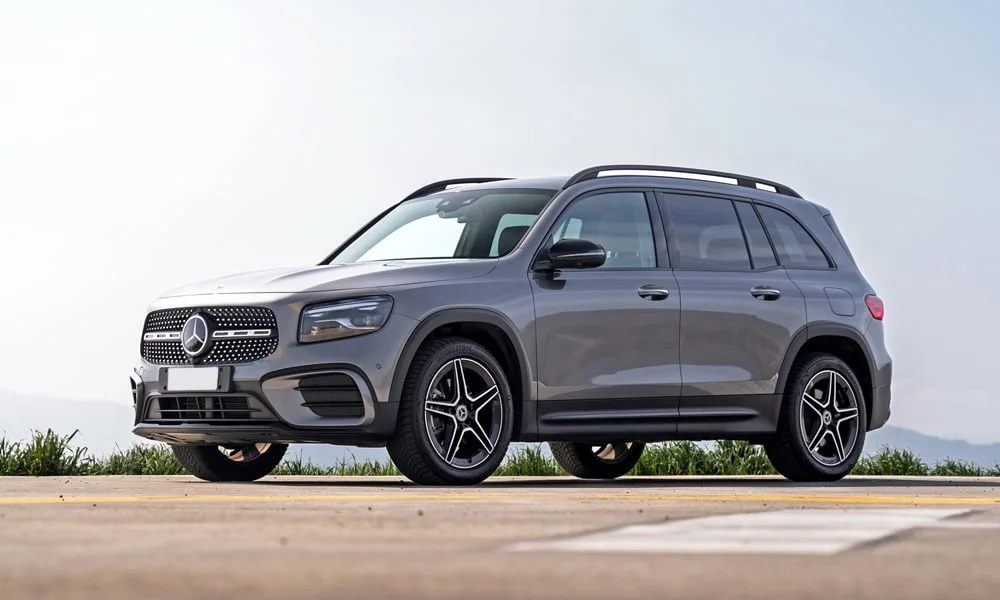 Фото Mercedes-Benz GLB (2024) — вид спереди. Серый кузов, строгая симметрия оптики — базовый ракурс знакомства с дизайном. Рисунок ходовых огней — подпись модели, по нему её узнают в потоке Mercedes-Benz GLB (2024) — вид спереди