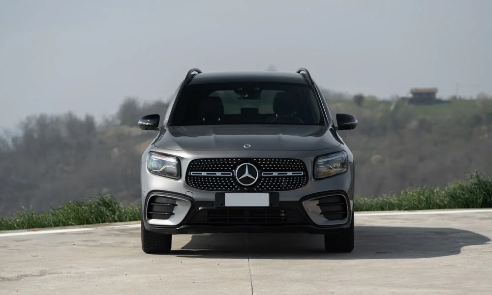 Фото Mercedes-Benz GLB (2024) — вид спереди, фото 2. Кузов в сером цвете: рисунок оптики и решётки задаёт узнаваемое «лицо» модели. Дневные ходовые огни включаются автоматически с запуском Mercedes-Benz GLB (2024) — вид спереди, фото 2