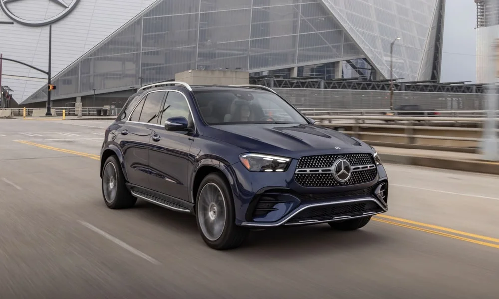 Фото Mercedes-Benz GLE (2024) — вид спереди, фото 11. Синий кузов, строгая симметрия оптики — базовый ракурс знакомства с дизайном. Рисунок ходовых огней — подпись модели, по нему её узнают в потоке Mercedes-Benz GLE (2024) — вид спереди, фото 11