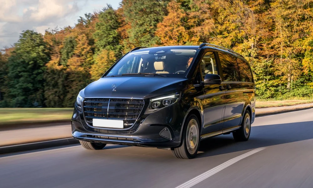 Фото Mercedes-Benz V-Class (2024) — вид спереди, фото 6. Чёрный кузов, строгая симметрия оптики — базовый ракурс знакомства с дизайном. Рисунок ходовых огней — подпись модели, по нему её узнают в потоке Mercedes-Benz V-Class (2024) — вид спереди, фото 6