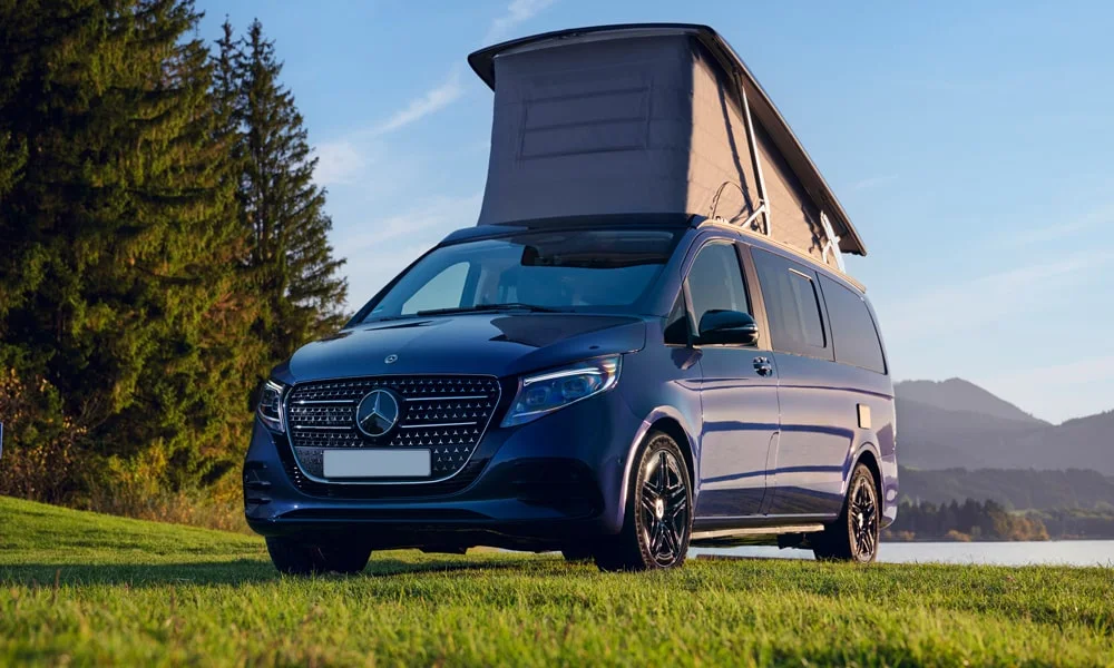 Фото Mercedes-Benz V-Class (2024) — вид спереди, фото 10. Кузов в синем цвете: рисунок оптики и решётки задаёт узнаваемое «лицо» модели. Рисунок ходовых огней — подпись модели, по нему её узнают в потоке Mercedes-Benz V-Class (2024) — вид спереди, фото 10