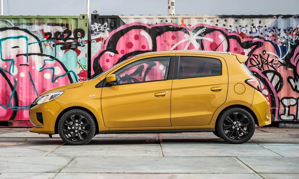 Фото Mitsubishi Space Star — вид сбоку, фото 2. Сбоку читаются линия остекления и характер выштамповок на жёлтом кузове. Хромированные или чёрные молдинги окон отличают комплектации Mitsubishi Space Star — вид сбоку, фото 2