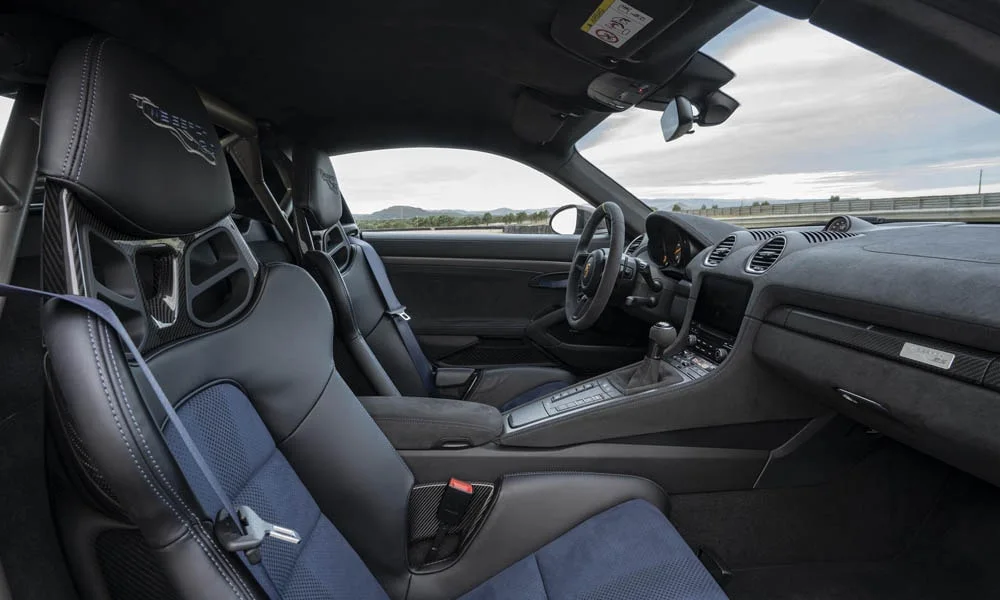 Фото Porsche 718 Cayman GT4 RS (2024) — интерьер. Общий план салона: посадка, материалы и организация пространства в тёмно-синей гамме. Светлая гамма зрительно расширяет салон, тёмная — практичнее в уходе Porsche 718 Cayman GT4 RS (2024) — интерьер