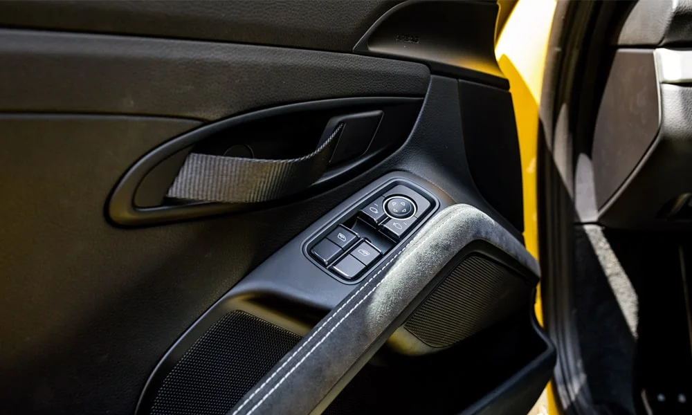 Фото Porsche 718 Cayman GT4 — дверная карта. Внутренняя панель двери: сочетание материалов и компоновка управления в тёмной гамме. Решётка динамика в двери — часть штатной акустики Porsche 718 Cayman GT4 — дверная карта
