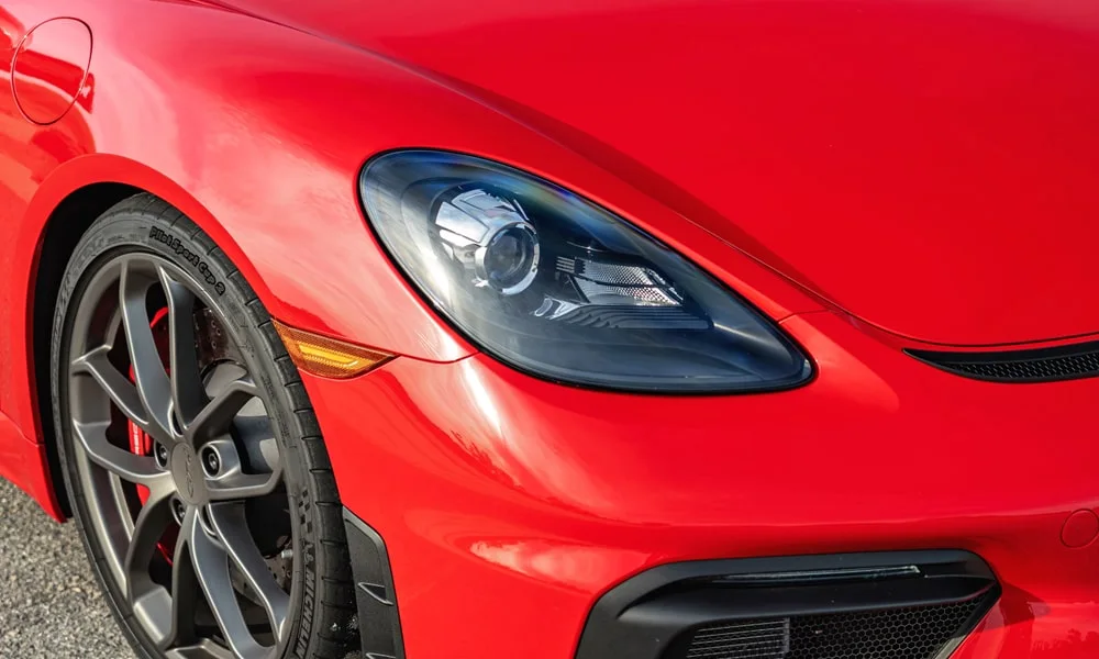 Фото Porsche 718 Cayman GT4 — вид спереди, фото 4. Кузов в красном цвете: рисунок оптики и решётки задаёт узнаваемое «лицо» модели. Дневные ходовые огни включаются автоматически с запуском Porsche 718 Cayman GT4 — вид спереди, фото 4