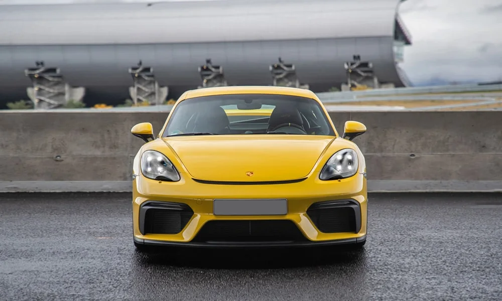 Фото Porsche 718 Cayman GT4 — вид спереди, фото 6. Жёлтый кузов, строгая симметрия оптики — базовый ракурс знакомства с дизайном. Рисунок ходовых огней — подпись модели, по нему её узнают в потоке Porsche 718 Cayman GT4 — вид спереди, фото 6