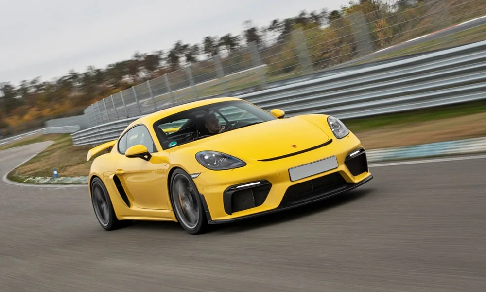Фото Porsche 718 Cayman GT4 — вид спереди, фото 8. Жёлтый кузов, строгая симметрия оптики — базовый ракурс знакомства с дизайном. Рисунок ходовых огней — подпись модели, по нему её узнают в потоке Porsche 718 Cayman GT4 — вид спереди, фото 8