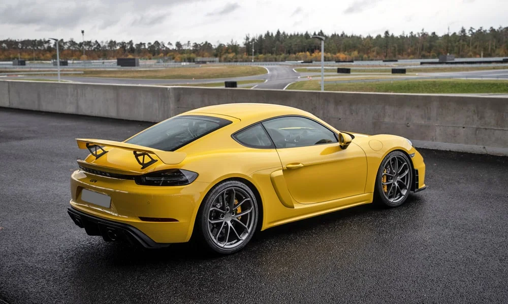 Фото Porsche 718 Cayman GT4 — вид сзади, фото 6. Линия крыши, стойки и задняя дверь в жёлтом исполнении. Насадки выхлопа или их имитация внизу бампера различают версии Porsche 718 Cayman GT4 — вид сзади, фото 6