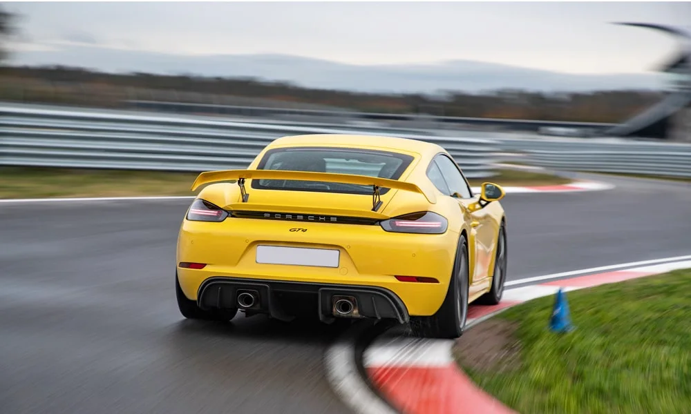 Фото Porsche 718 Cayman GT4 — вид сзади, фото 7. Линия крыши, стойки и задняя дверь в жёлтом исполнении. Насадки выхлопа или их имитация внизу бампера различают версии Porsche 718 Cayman GT4 — вид сзади, фото 7