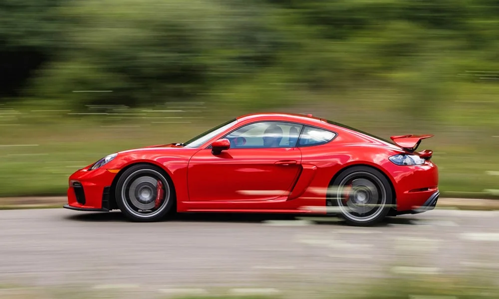 Фото Porsche 718 Cayman GT4 — вид сбоку. Красный кузов в профиль — пропорции, высота посадки и дизайн дисков. Длинная база — простор второго ряда; короткие свесы упрощают парковку Porsche 718 Cayman GT4 — вид сбоку