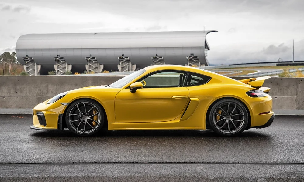 Фото Porsche 718 Cayman GT4 — вид сбоку, фото 2. Сбоку читаются линия остекления и характер выштамповок на жёлтом кузове. Длинная база — простор второго ряда; короткие свесы упрощают парковку Porsche 718 Cayman GT4 — вид сбоку, фото 2