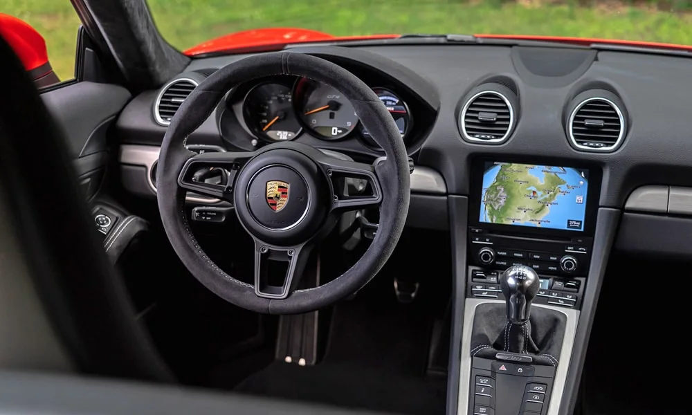 Фото Porsche 718 Cayman GT4 — руль. Обшивка обода и компоновка спиц крупным планом. Клавиши на спицах управляют медиа, круизом и ассистентами — руки остаются на руле Porsche 718 Cayman GT4 — руль
