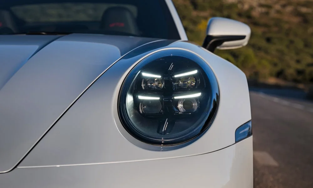 Фото Porsche 911 — вид спереди, фото 18. Передок в белом исполнении — крупная светотехника и выразительный бампер. Рисунок ходовых огней — подпись модели, по нему её узнают в потоке Porsche 911 — вид спереди, фото 18