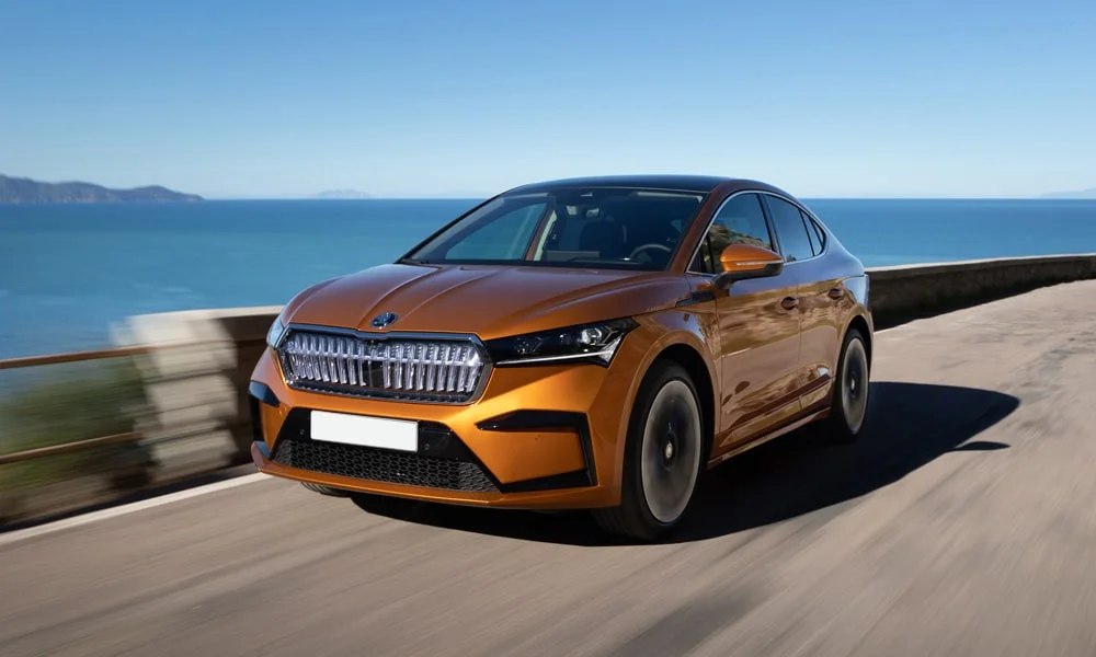 Фото Skoda Enyaq Coupe (2024) — вид спереди, фото 7. Кузов в оранжевом цвете: рисунок оптики и решётки задаёт узнаваемое «лицо» модели. Дневные ходовые огни включаются автоматически с запуском Skoda Enyaq Coupe (2024) — вид спереди, фото 7