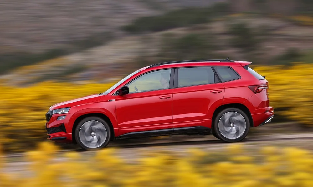 Фото Skoda Karoq (2024) — вид сбоку, фото 3. Сбоку читаются линия остекления и характер выштамповок на красном кузове. Длинная база — простор второго ряда; короткие свесы упрощают парковку Skoda Karoq (2024) — вид сбоку, фото 3