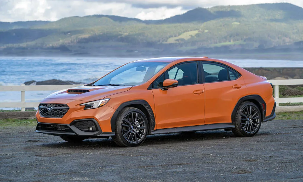 Фото Subaru WRX STI (2024) — вид спереди, фото 8. Кузов в оранжевом цвете: рисунок оптики и решётки задаёт узнаваемое «лицо» модели. Рисунок ходовых огней — подпись модели, по нему её узнают в потоке Subaru WRX STI (2024) — вид спереди, фото 8