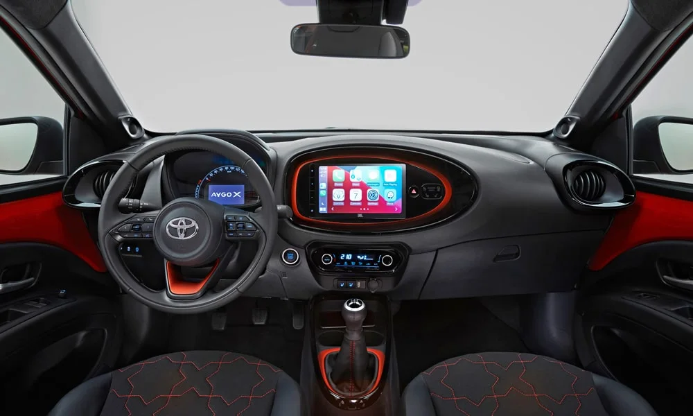 Фото Toyota Aygo X — передняя панель. Передняя панель в красно-чёрной отделке: расположение экранов и дефлекторов. Мягкие материалы верхнего яруса и вставки задают уровень интерьера Toyota Aygo X — передняя панель