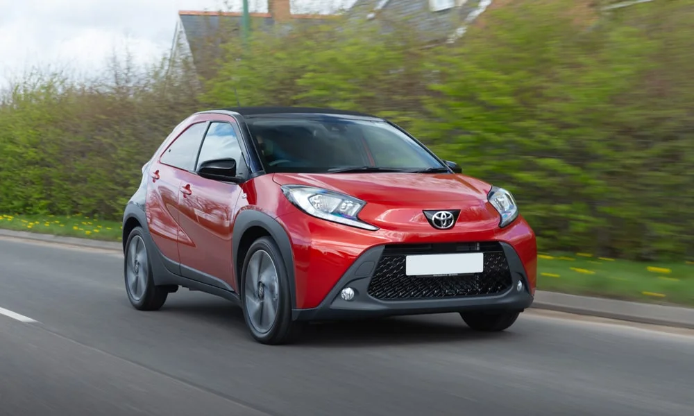 Фото Toyota Aygo X — вид спереди, фото 6. Красный кузов, строгая симметрия оптики — базовый ракурс знакомства с дизайном. Дневные ходовые огни включаются автоматически с запуском Toyota Aygo X — вид спереди, фото 6