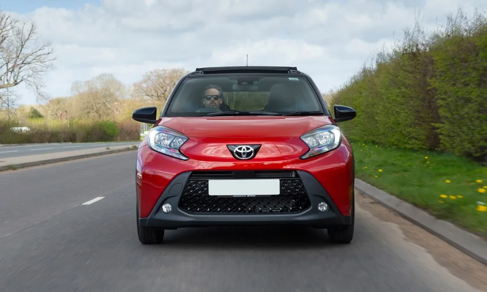 Фото Toyota Aygo X — вид спереди, фото 8. Красный кузов, строгая симметрия оптики — базовый ракурс знакомства с дизайном Toyota Aygo X — вид спереди, фото 8