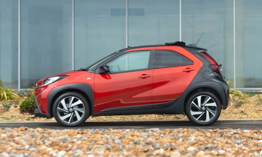 Фото Toyota Aygo X — вид сбоку, фото 3. Красный кузов в профиль — пропорции, высота посадки и дизайн дисков. Длинная база — простор второго ряда; короткие свесы упрощают парковку Toyota Aygo X — вид сбоку, фото 3