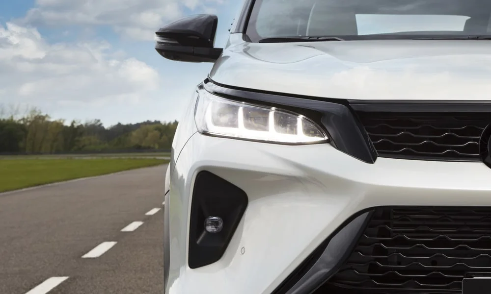Фото Toyota Fortuner (2024) — вид спереди, фото 9. Передок в белом исполнении — крупная светотехника и выразительный бампер. Дневные ходовые огни включаются автоматически с запуском Toyota Fortuner (2024) — вид спереди, фото 9