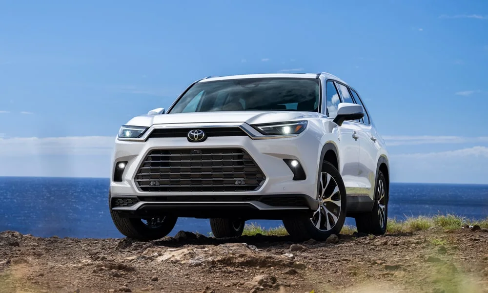 Фото Toyota Grand Highlander (2024) — вид спереди, фото 8. Кузов в белом цвете: рисунок оптики и решётки задаёт узнаваемое «лицо» модели. Рисунок ходовых огней — подпись модели, по нему её узнают в потоке Toyota Grand Highlander (2024) — вид спереди, фото 8