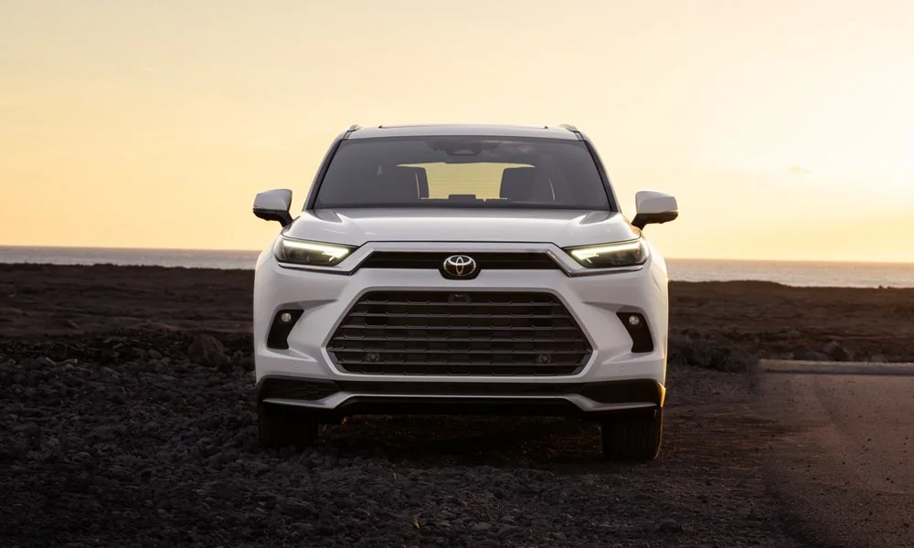 Фото Toyota Grand Highlander (2024) — вид спереди, фото 11. Белый кузов, строгая симметрия оптики — базовый ракурс знакомства с дизайном. Рисунок ходовых огней — подпись модели, по нему её узнают в потоке Toyota Grand Highlander (2024) — вид спереди, фото 11