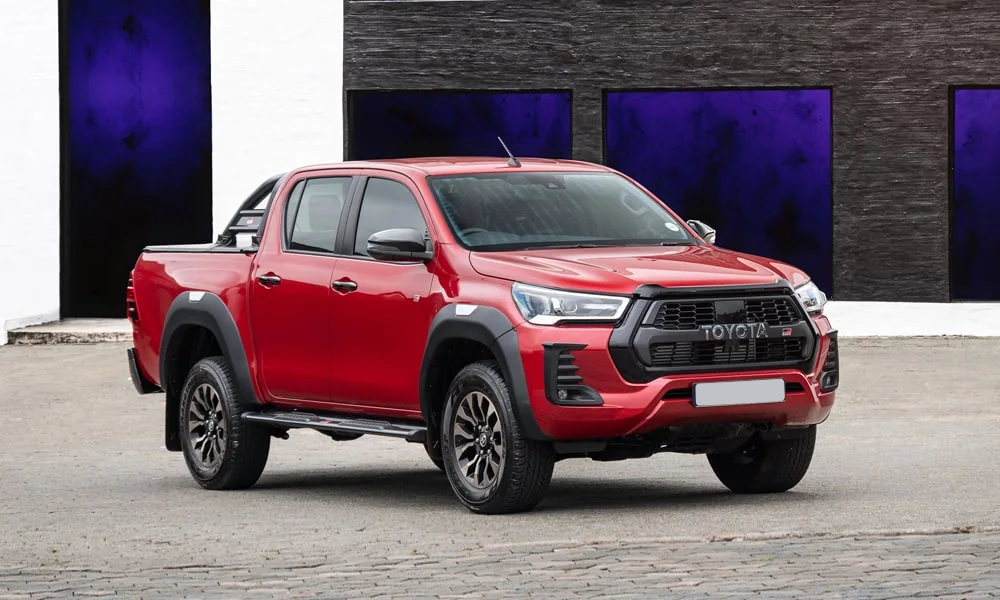 Фото Toyota Hilux (2024) — вид спереди, фото 9. Красный кузов, строгая симметрия оптики — базовый ракурс знакомства с дизайном. Рисунок ходовых огней — подпись модели, по нему её узнают в потоке Toyota Hilux (2024) — вид спереди, фото 9