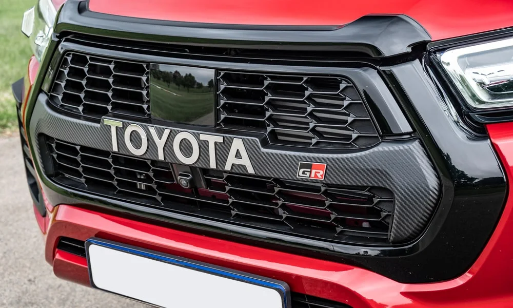 Фото Toyota Hilux (2024) — решётка радиатора. Рисунок решётки: сетка, ламели или глухая панель у электроверсий. Активные жалюзи за решёткой закрываются на трассе ради аэродинамики — есть у ряда моделей Toyota Hilux (2024) — решётка радиатора