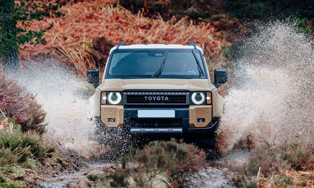 Фото Toyota Land Cruiser Prado (2024) — вид спереди, фото 10. Бежевый кузов, строгая симметрия оптики — базовый ракурс знакомства с дизайном. Дневные ходовые огни включаются автоматически с запуском Toyota Land Cruiser Prado (2024) — вид спереди, фото 10