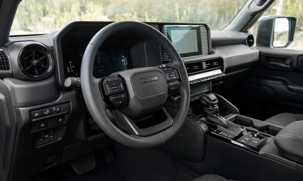 Фото Toyota Land Cruiser Prado (2024) — интерьер, фото 2. Общий план салона: архитектура панели, консоль и кресла. Светлая гамма зрительно расширяет салон, тёмная — практичнее в уходе Toyota Land Cruiser Prado (2024) — интерьер, фото 2