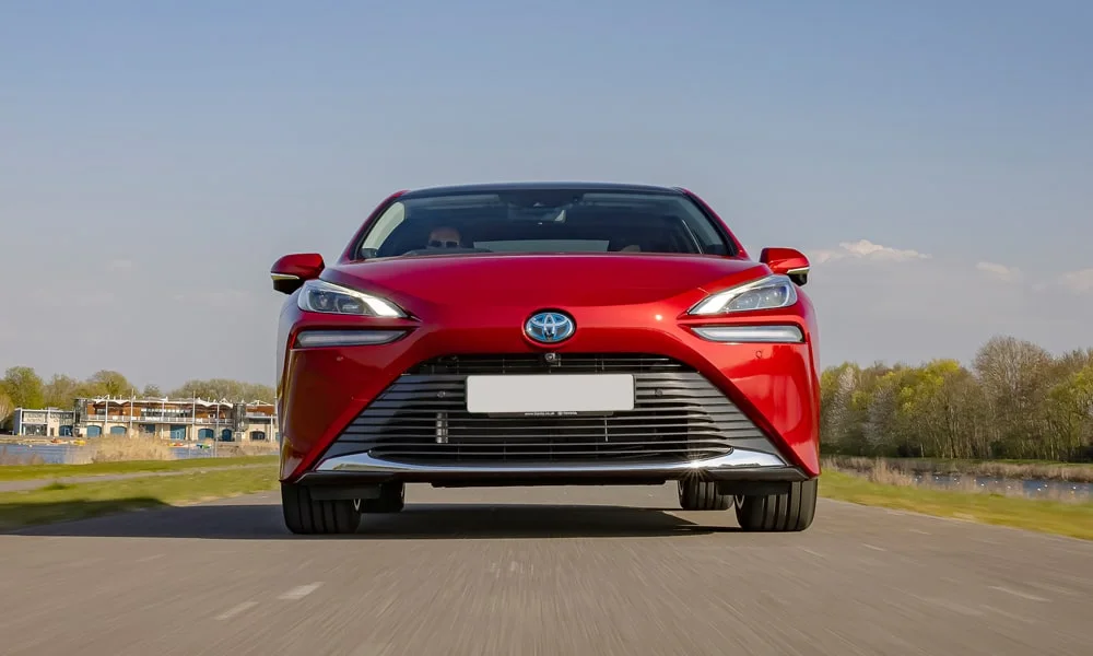 Фото Toyota Mirai (2024) — вид спереди, фото 7. Передок в красном исполнении — крупная светотехника и выразительный бампер. Рисунок ходовых огней — подпись модели, по нему её узнают в потоке Toyota Mirai (2024) — вид спереди, фото 7