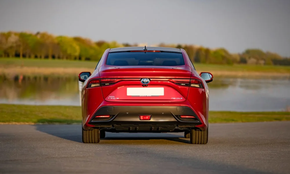 Фото Toyota Mirai (2024) — вид сзади, фото 2. Линия крыши, стойки и задняя дверь в красном исполнении. Насадки выхлопа или их имитация внизу бампера различают версии Toyota Mirai (2024) — вид сзади, фото 2