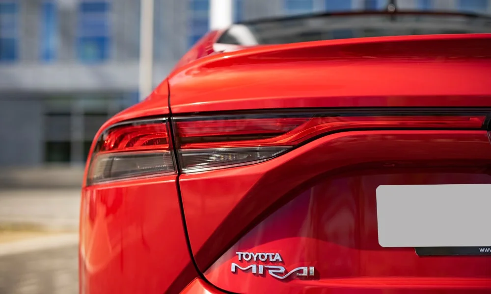 Фото Toyota Mirai (2024) — вид сзади, фото 3. Корма в красном цвете: графика фонарей и пластика пятой двери. Светодиодная полоса или раздельные секции — задняя оптика стала главным украшением кормы Toyota Mirai (2024) — вид сзади, фото 3