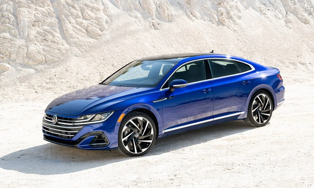 Фото Volkswagen Arteon (2024) — вид спереди, фото 11. Синий кузов, строгая симметрия оптики — базовый ракурс знакомства с дизайном. Рисунок ходовых огней — подпись модели, по нему её узнают в потоке Volkswagen Arteon (2024) — вид спереди, фото 11