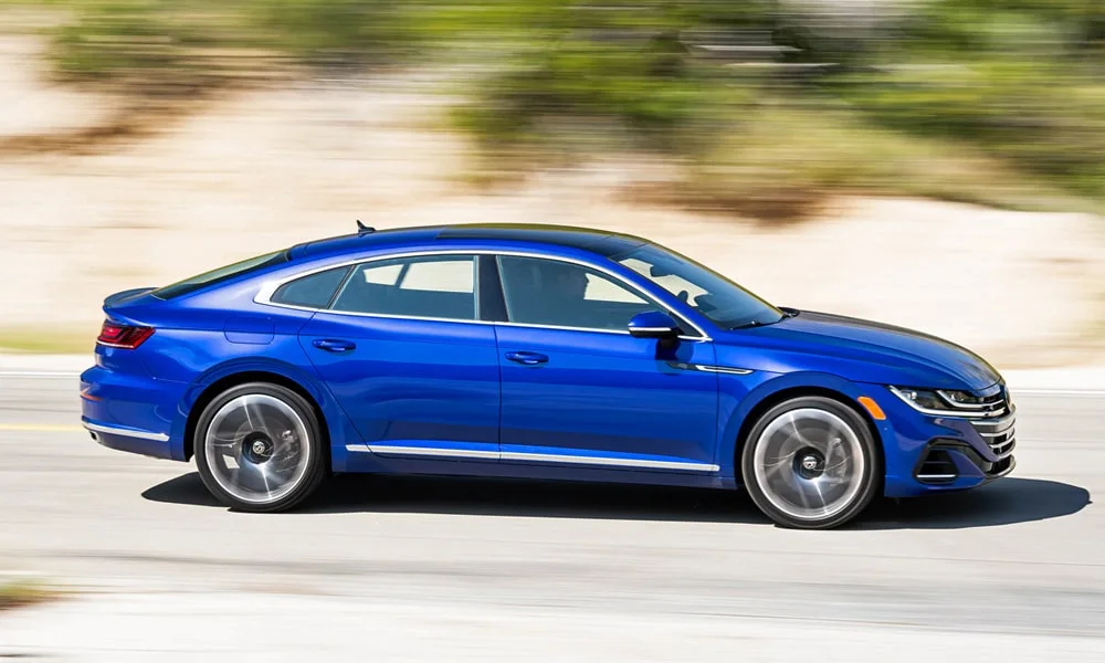 Фото Volkswagen Arteon (2024) — вид сбоку, фото 3. Сбоку читаются линия остекления и характер выштамповок на синем кузове. Хромированные или чёрные молдинги окон отличают комплектации Volkswagen Arteon (2024) — вид сбоку, фото 3