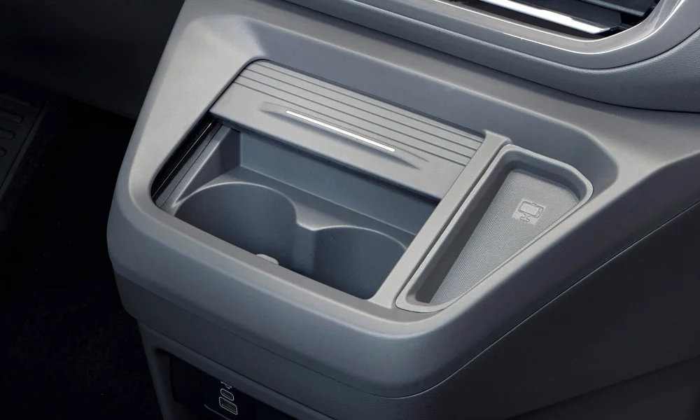Фото Volkswagen Caravelle (2024) — центральная консоль. Подстаканники и ниши для мелочей между креслами. Прорезиненное дно ниш удерживает мелочи в поворотах Volkswagen Caravelle (2024) — центральная консоль