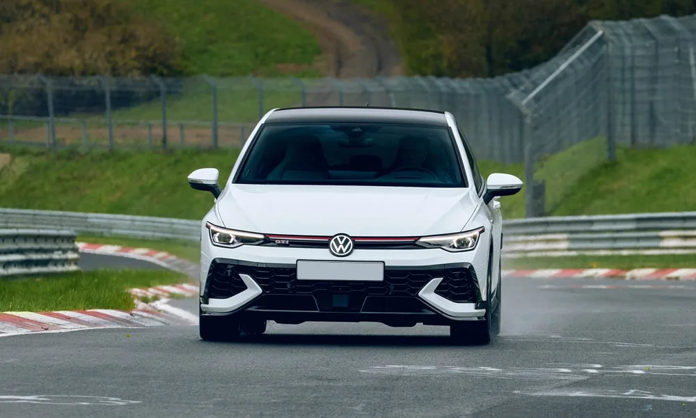 Фото Volkswagen Golf GTI (2024) — вид спереди, фото 5. Белый кузов, строгая симметрия оптики — базовый ракурс знакомства с дизайном. Рисунок ходовых огней — подпись модели, по нему её узнают в потоке Volkswagen Golf GTI (2024) — вид спереди, фото 5
