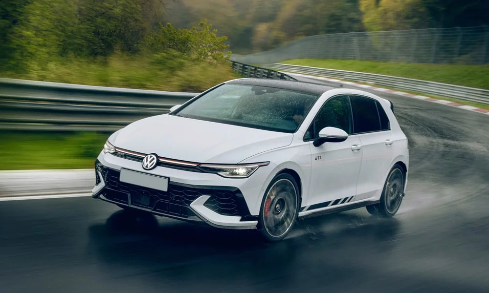 Фото Volkswagen Golf GTI (2024) — вид спереди, фото 6. Белый кузов, строгая симметрия оптики — базовый ракурс знакомства с дизайном. Рисунок ходовых огней — подпись модели, по нему её узнают в потоке Volkswagen Golf GTI (2024) — вид спереди, фото 6