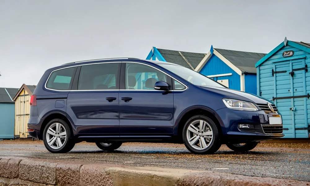 Фото Volkswagen Sharan — вид сбоку, фото 6. Сбоку читаются линия остекления и характер выштамповок на синем кузове. Хромированные или чёрные молдинги окон отличают комплектации Volkswagen Sharan — вид сбоку, фото 6