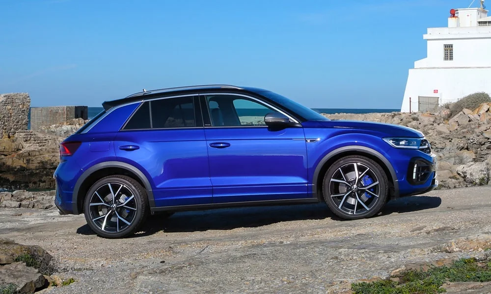 Фото Volkswagen T-Roc — вид сбоку. Сбоку читаются линия остекления и характер выштамповок на синем кузове. Хромированные или чёрные молдинги окон отличают комплектации Volkswagen T-Roc — вид сбоку