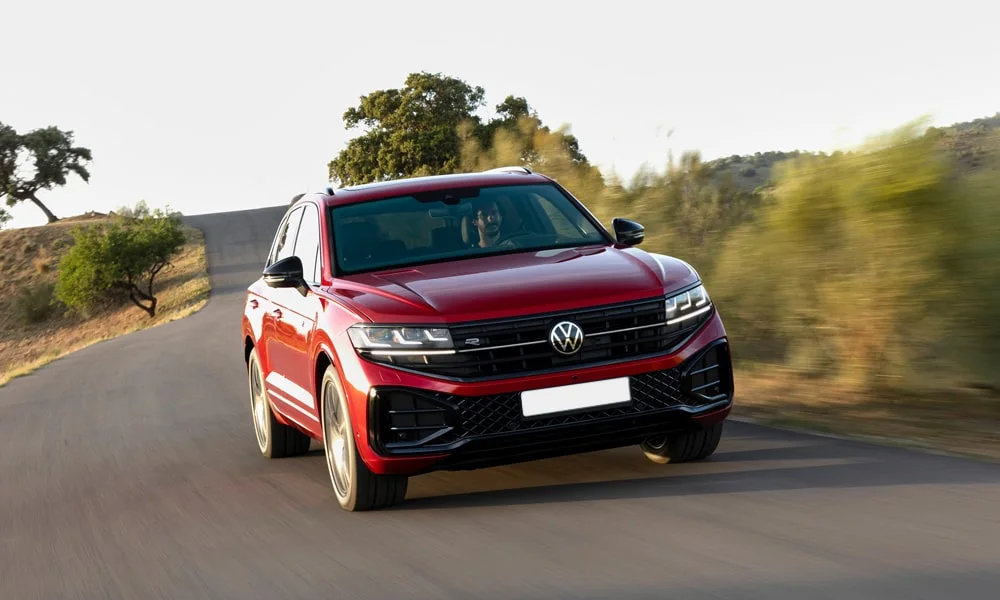 Фото Volkswagen Touareg (2024) — вид спереди, фото 10. Красный кузов, строгая симметрия оптики — базовый ракурс знакомства с дизайном. Рисунок ходовых огней — подпись модели, по нему её узнают в потоке Volkswagen Touareg (2024) — вид спереди, фото 10