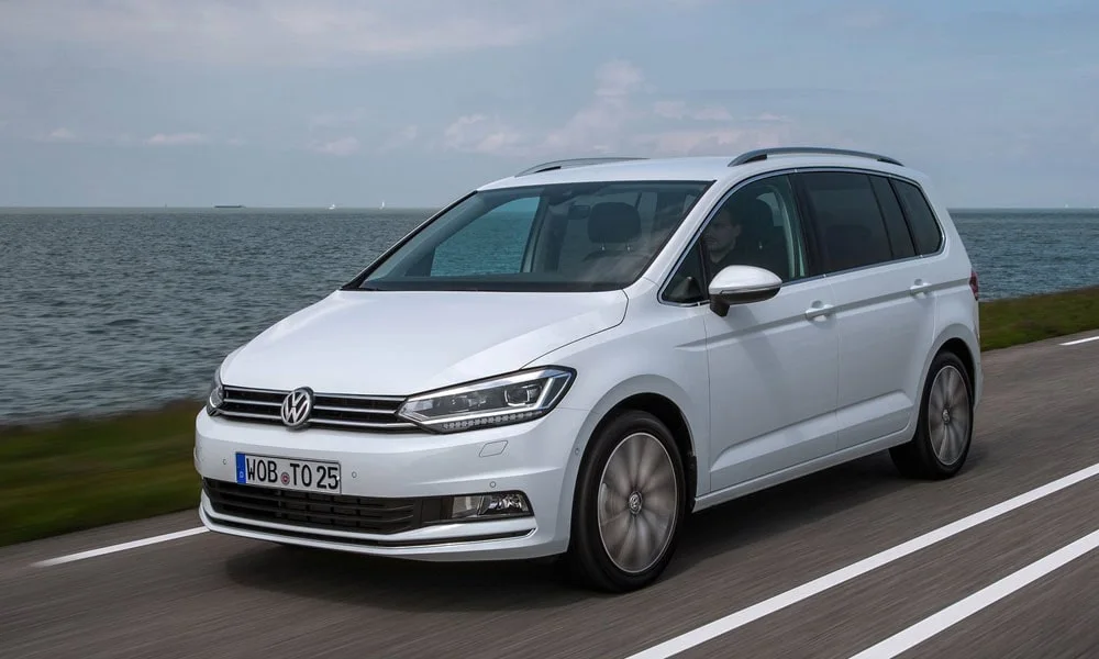 Фото Volkswagen Touran — вид спереди, фото 8. Белый кузов, строгая симметрия оптики — базовый ракурс знакомства с дизайном. Дневные ходовые огни включаются автоматически с запуском Volkswagen Touran — вид спереди, фото 8