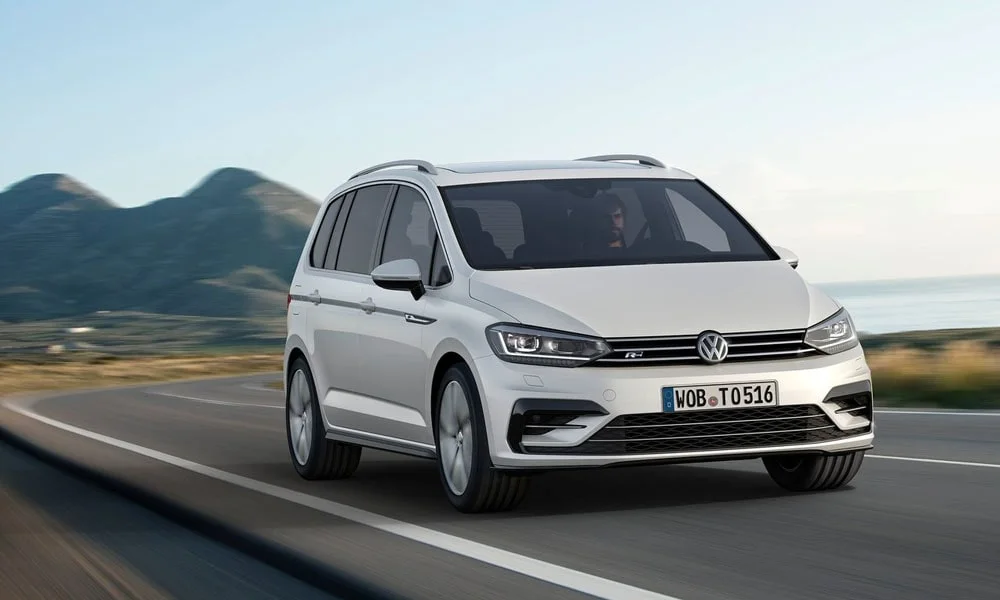 Фото Volkswagen Touran — вид спереди, фото 11. Белый кузов, строгая симметрия оптики — базовый ракурс знакомства с дизайном. Рисунок ходовых огней — подпись модели, по нему её узнают в потоке Volkswagen Touran — вид спереди, фото 11
